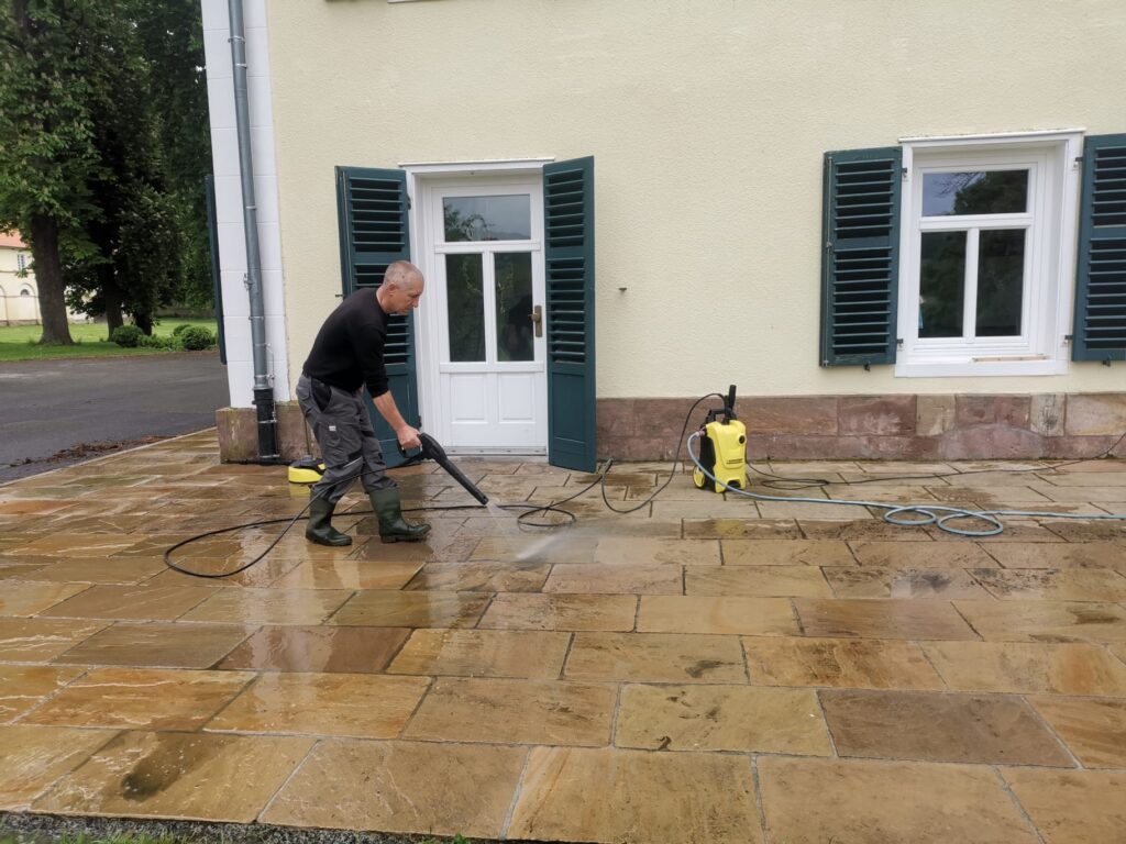 Mitarbeiter von AKTIV Team reinigt eine Natursteinterrasse mit dem Hochdruckreiniger