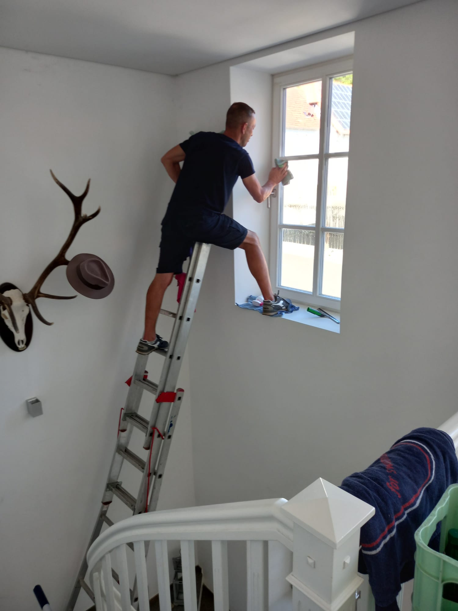 Mitarbeiter reinigt ein Treppenhausfenster von der Leiter aus